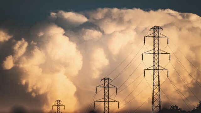 High voltage power lines and towers silhouetted against large dramatic clouds in a rural field setting.