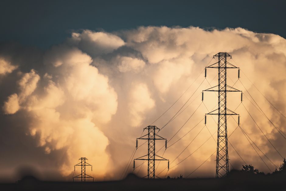 High voltage power lines and towers silhouetted against large dramatic clouds in a rural field setting.