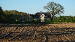 Modern house with solar panels surrounded by field and trees on a clear spring day.