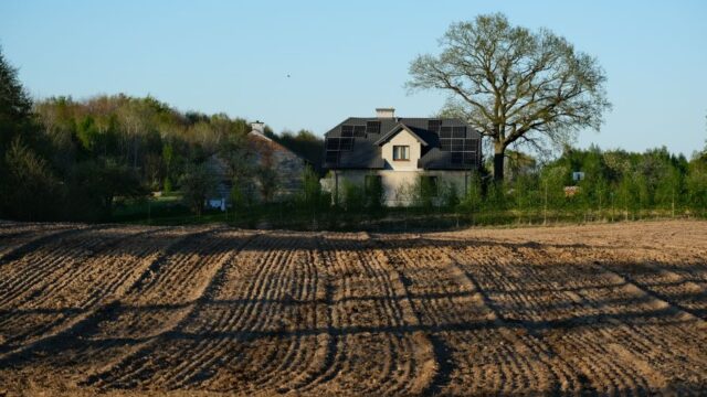 Modern house with solar panels surrounded by field and trees on a clear spring day.
