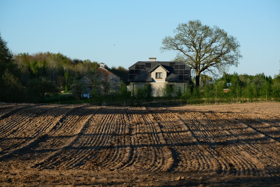 Modern house with solar panels surrounded by field and trees on a clear spring day.