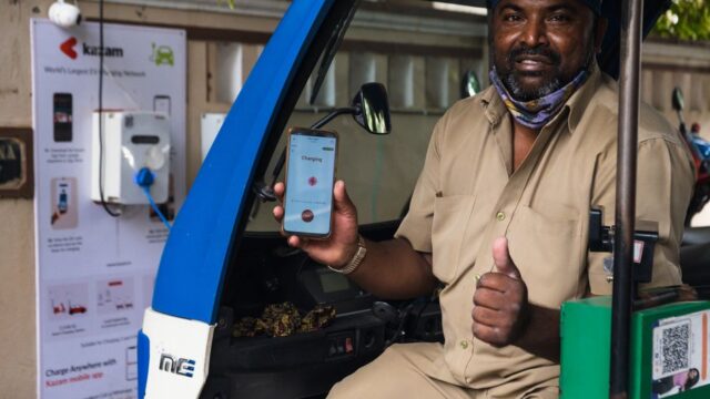 South Asian man using electric vehicle charging station in India, holding smartphone with app.