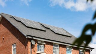 Brick house featuring solar panels on the roof under a clear blue sky, promoting sustainable energy.