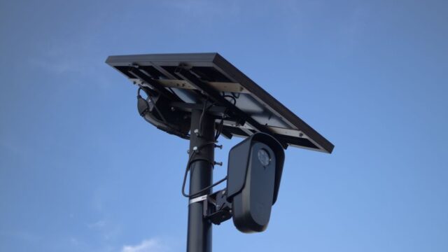 Solar-powered surveillance camera with a clear blue sky backdrop, highlighting modern technology.