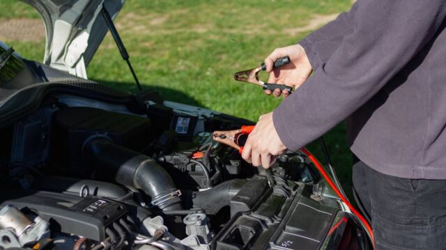 Close-up of mechanic using jumper cables to jump-start a car battery outdoors.