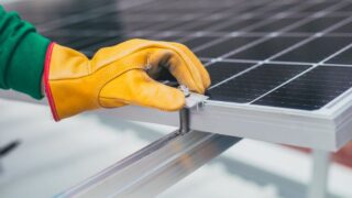Close-up of a worker's hand with protective gloves adjusting a bolt on a solar panel.