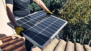 A worker installs a solar panel on a rooftop amidst lush greenery.