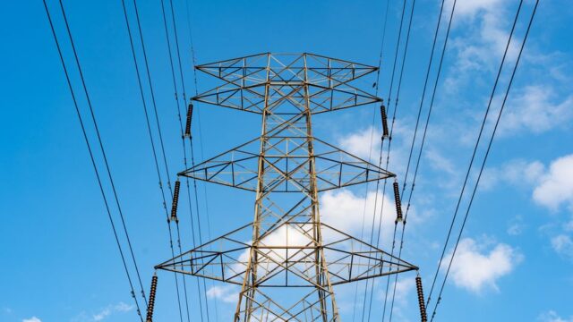 Industrial scene with a high voltage power line tower against a clear blue sky.