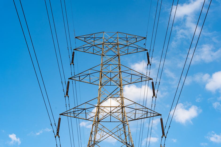 Industrial scene with a high voltage power line tower against a clear blue sky.