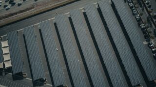 An aerial view showcasing a solar farm with aligned solar panels next to a busy parking lot.