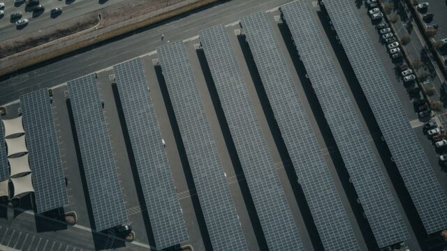 An aerial view showcasing a solar farm with aligned solar panels next to a busy parking lot.