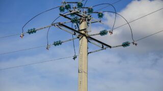 A high voltage power line stretching against a clear blue sky with clouds.