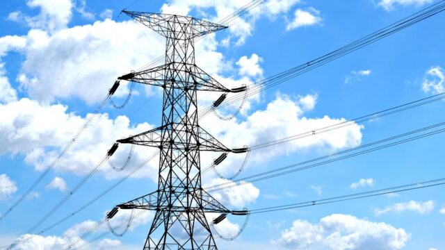 Electricity pylon with high voltage lines set against a vibrant blue sky with clouds.