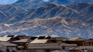 Residential area with houses and solar panels set against scenic mountains.