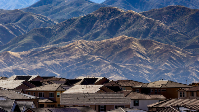 Residential area with houses and solar panels set against scenic mountains.