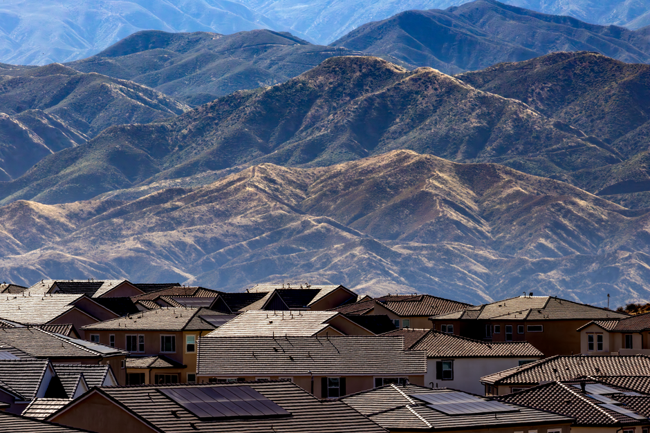Residential area with houses and solar panels set against scenic mountains.