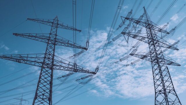 High voltage transmission towers stretch across a clear blue sky, symbolizing energy and industry.