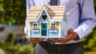 A businessman holds a detailed, colorful miniature house model. Ideal for concepts of real estate and property investment.