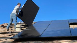 A worker installs solar panels on a sunny day, highlighting renewable energy solutions.