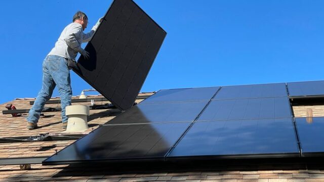 A worker installs solar panels on a sunny day, highlighting renewable energy solutions.