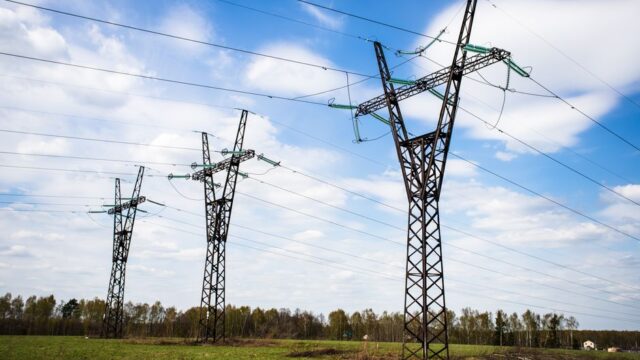 High voltage electric towers stand tall over a clear sky and grassy field, providing a serene landscape view.