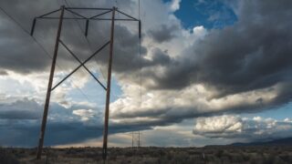 Dramatic landscape with high voltage power lines beneath a cloudy sky, showcasing energy infrastructure in an open field.