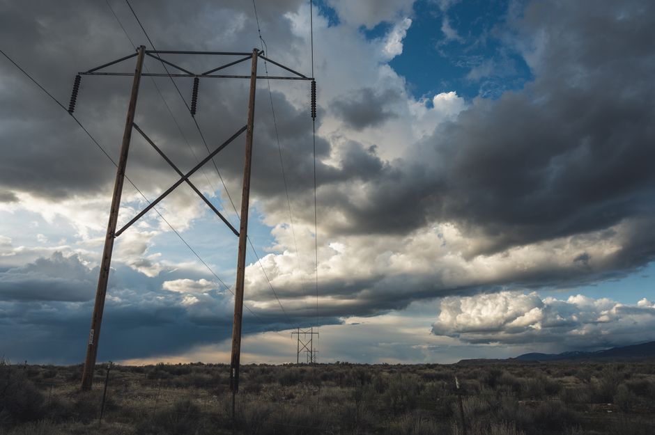 Dramatic landscape with high voltage power lines beneath a cloudy sky, showcasing energy infrastructure in an open field.