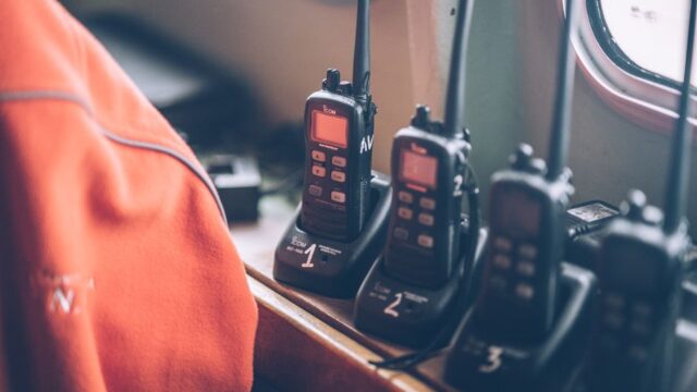 Four wireless walkie talkies in charging stations on a wooden dock indoors.