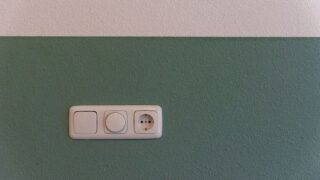 Close-up of a power outlet and switch on a textured green wall indoors.