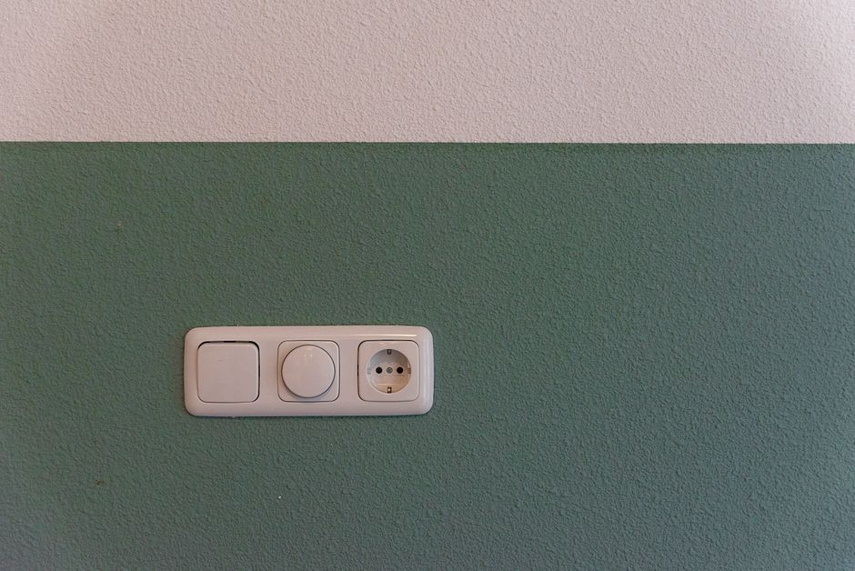 Close-up of a power outlet and switch on a textured green wall indoors.