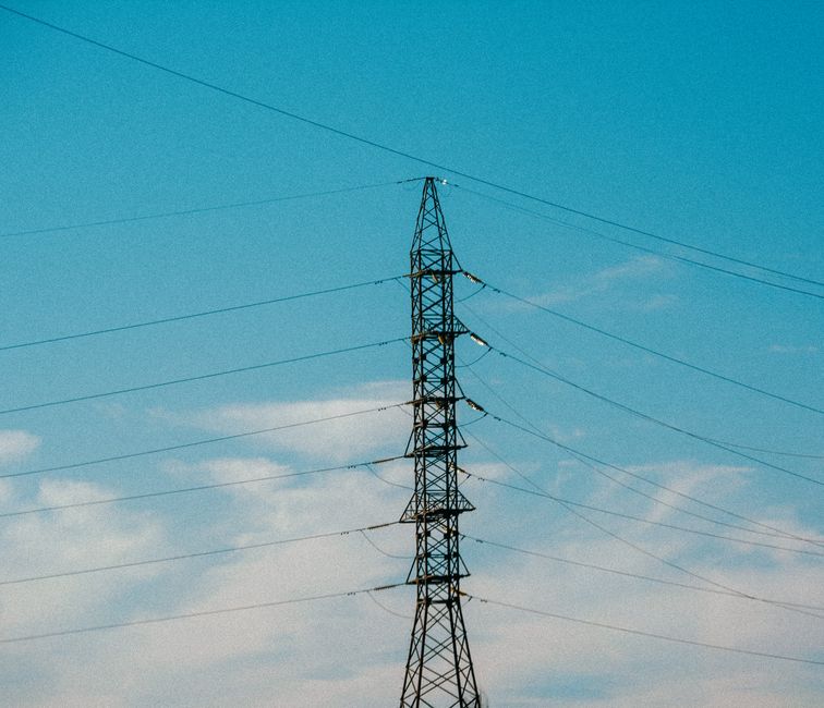 High voltage power lines stretching into blue sky with scattered clouds.