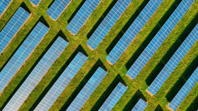 High-angle aerial shot of solar panels in a lush green field, located in Rockbeare, UK.