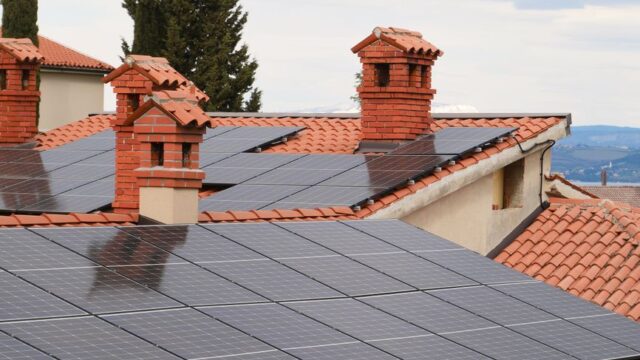 Solar panels on tiled roofs of houses with chimneys, capturing clean energy.